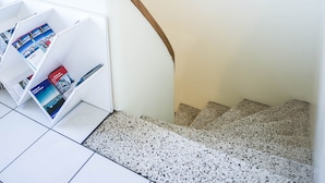 Un escalier avec un sol carrelé de carreaux blancs et un luminaire au plafond blanc, à texture.
