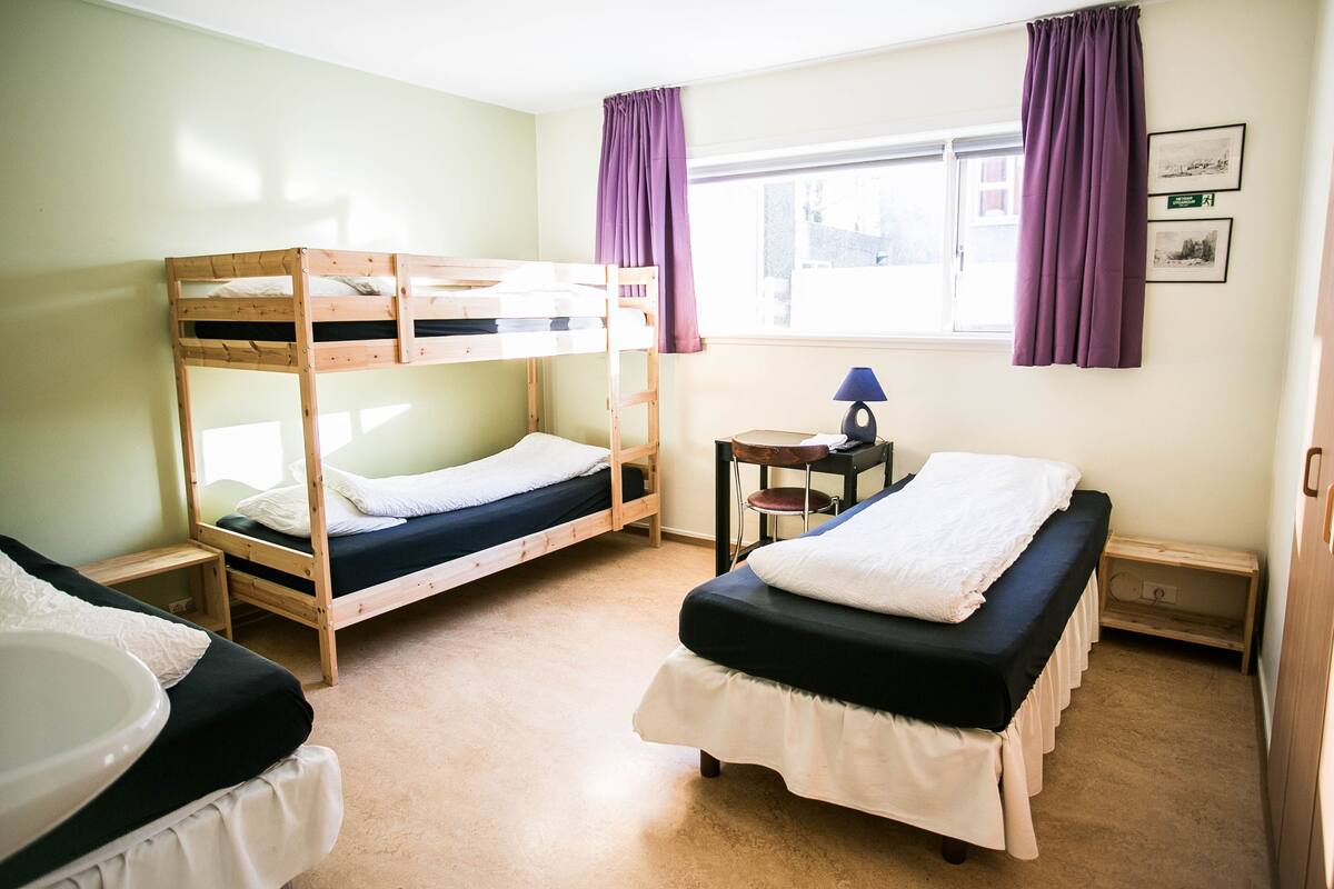 Une chambre avec des lits superposés, une petite table avec une lampe et une fenêtre avec des rideaux.
