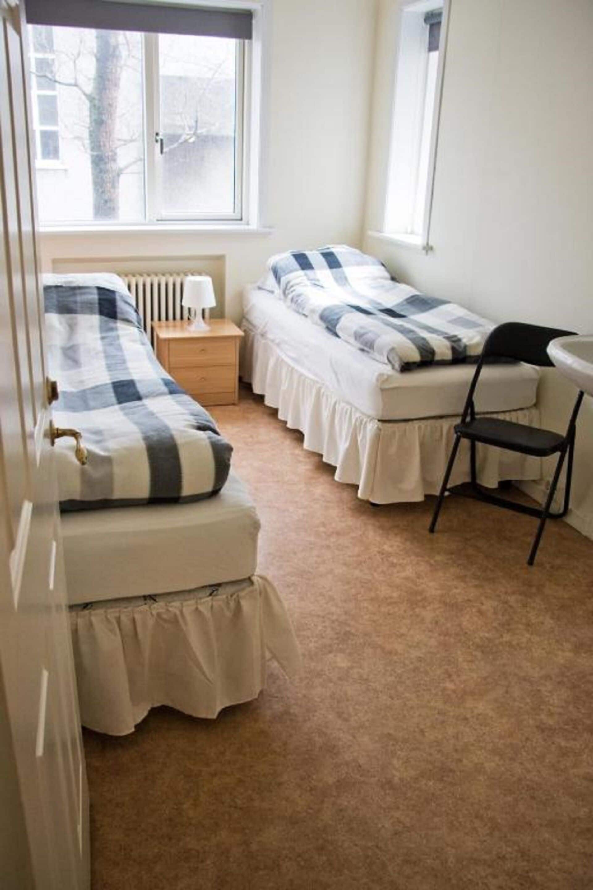 Une petite chambre confortable avec deux lits, une chaise et une table de chevet.