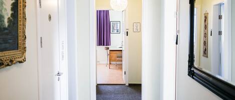 Un pasillo con piso alfombrado, paredes blancas y una puerta que da a una habitación con cortina púrpura.