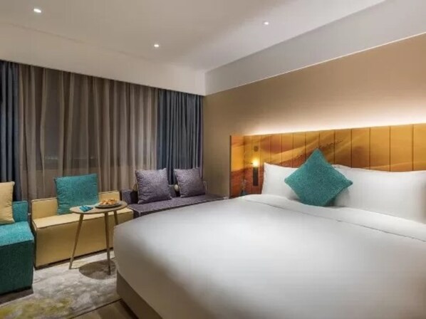 Una habitación de hotel moderna con una cama grande, una zona de estar con una mesita y un ventanal con cortinas.