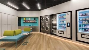 A modern hotel room with a wooden floor, a seating area with green cushions, a washing machine, and a beverage vending machine. - Manxin Hotel Xian North Railway Station Municipal Government (Xi'an)