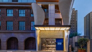 A modern hotel entrance with a prominent archway, a blue sign, and a staircase leading to the entrance. - Manxin Hotel Xian North Railway Station Municipal Government (Xi'an)