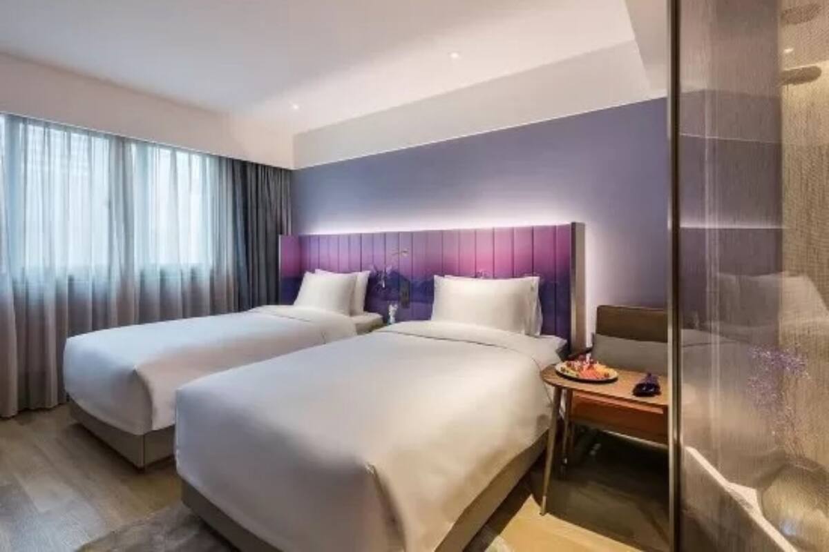 A hotel room with two beds, a nightstand, and a glass shower enclosure.