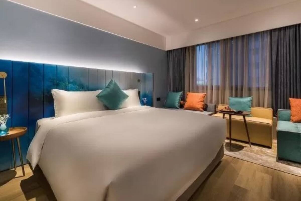 A modern hotel room with a large bed, a small sofa, and a nightstand.