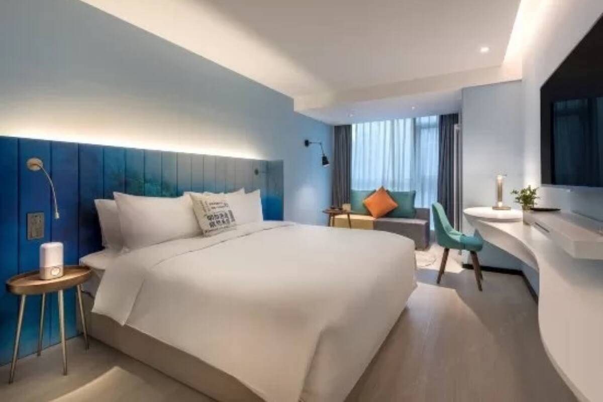 A modern hotel room with a large bed, a desk, and a seating area.