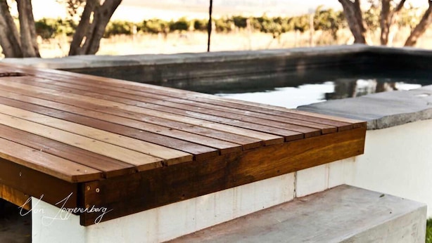 A wooden deck with a concrete edge, overlooking a body of water and trees. - Denneboom Vineyards and Wildlife (Paarl)