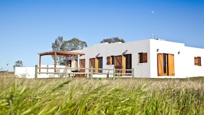 A white building with wooden doors and windows, a covered patio, and a fence. - Denneboom Vineyards and Wildlife (Paarl)
