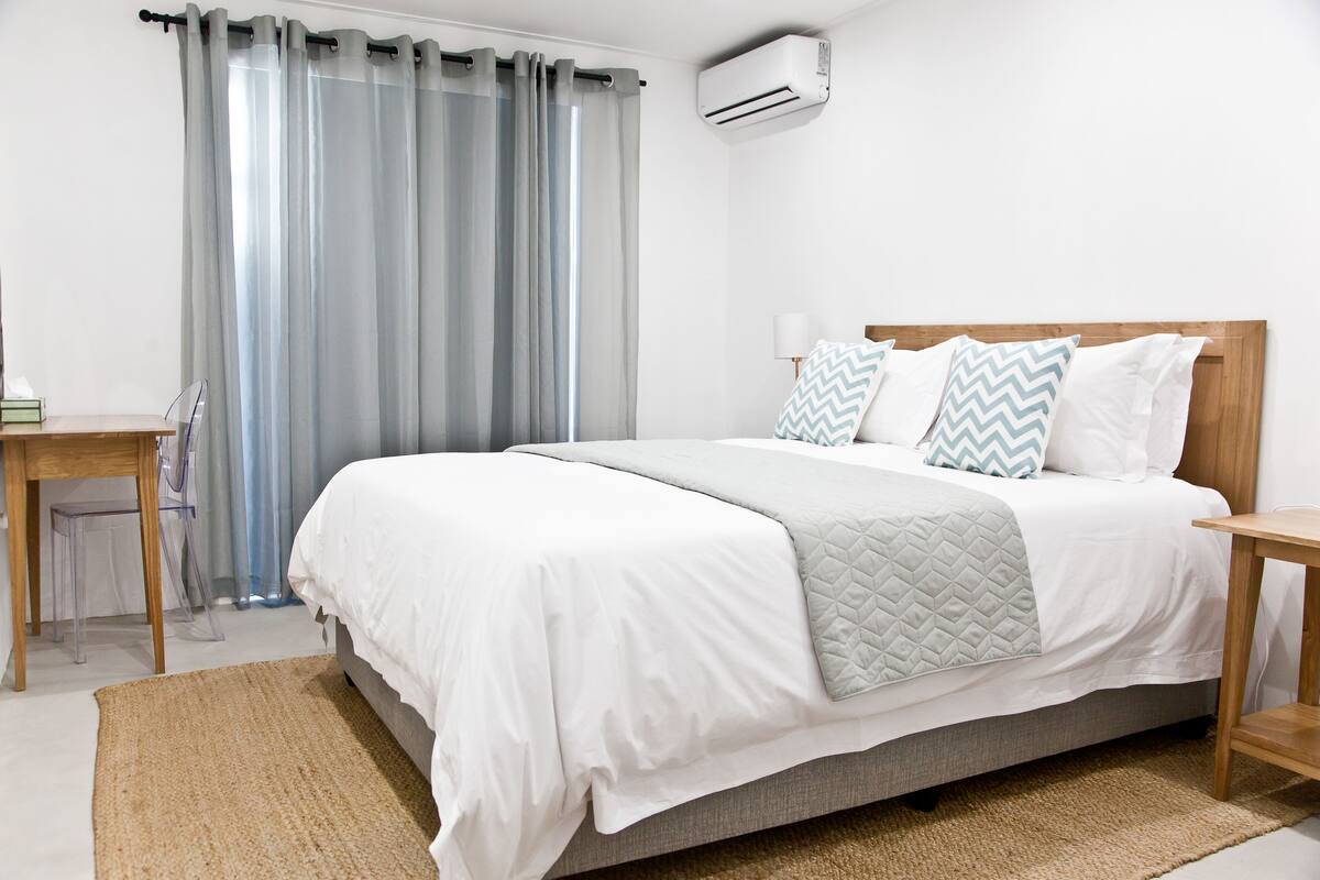 A neatly arranged bedroom with a bed, bedside tables, a desk, and a chair.