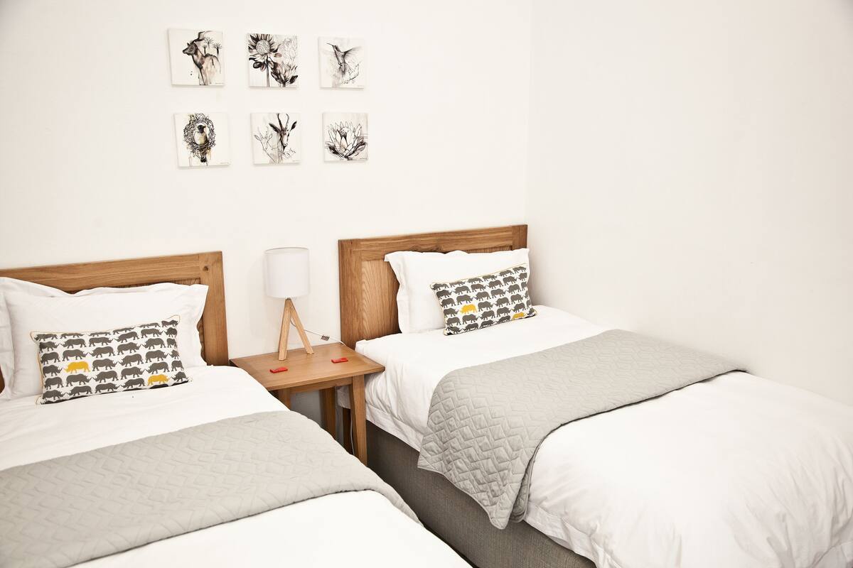 A hotel room with two beds, a bedside table with a lamp, and wall art.