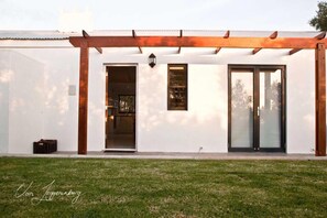A modern building with a white exterior, a wooden pergola, and a large sliding glass door.