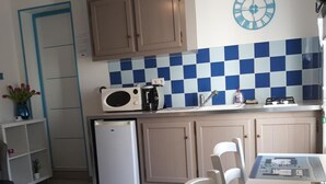 Cocina compacta con refrigerador, microondas y estufa. Hay una mesa de comedor con sillas y un reloj decorativo en la pared.