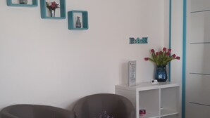 Una sala de estar moderna con un sofá gris, una mesa de centro negra redonda con un jarrón blanco y un estante blanco con objetos decorativos.
