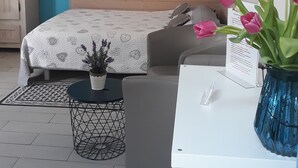 Un dormitorio con una cama, un escritorio, una silla, una mesita con una planta y un jarrón con flores.