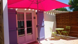 Un patio con un paraguas rosa, una cerca de madera y dos sillas verdes.