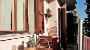 Un patio al aire libre con una mesa y sillas de madera, una planta colgante y una ventana con cortinas.