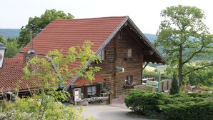 Ein rustikales Holzgebäude mit rotem Ziegeldach, einem Steinsschornstein und einem gepflasterten Eingang.