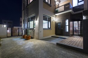 A modern building with a well-lit entrance, a wooden deck, and potted plants. - Spring Villa (Magong)
