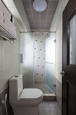 A modern bathroom with a toilet, a glass shower enclosure, and a dark wooden door. - Spring Villa (Magong)