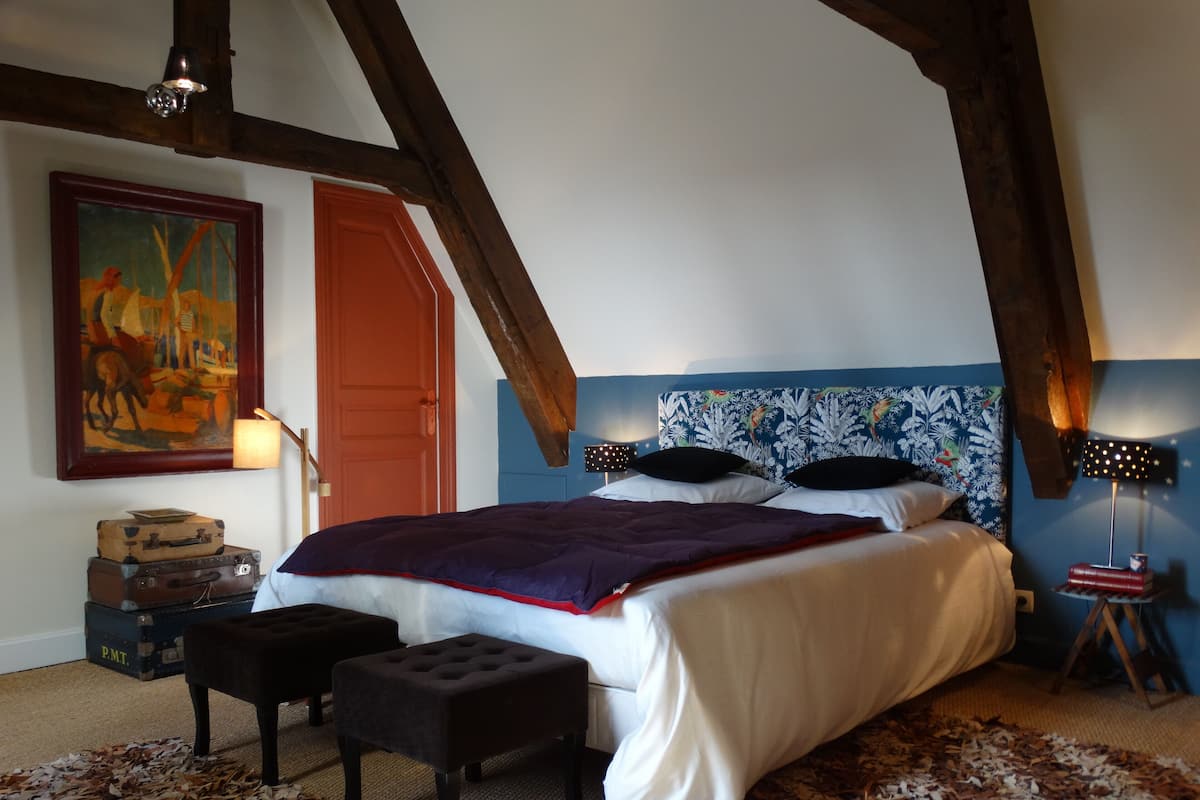 Een slaapkamer met een bed, nachtkastje, schilderij en houten plafond.