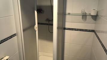 Un baño con cabina de ducha de vidrio, inodoro y repisa con artículos de aseo.
