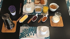 Une table de petit-déjeuner dressée avec des assiettes, des couverts, une cafetière, un pichet et un bol de céréales.