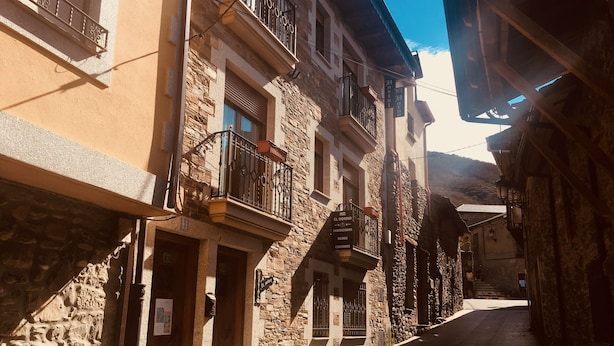 Une rue étroite bordée d’immeubles en pierre, de balcons ornés de rampes en fer forgé et d’un ciel dégagé.