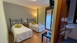 Une chambre d’hôtel avec deux lits simples, une petite table, une télévision et une salle de bain avec un lavabo.