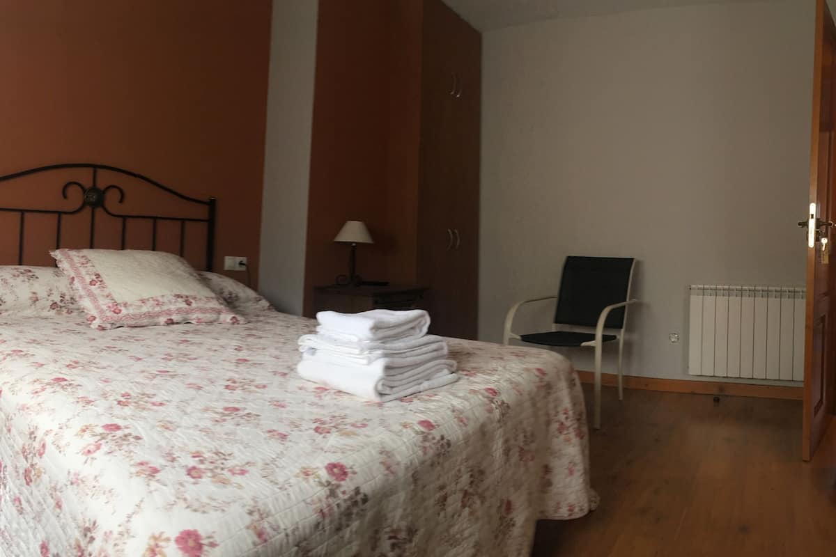 Um quarto com cama, uma cadeira, um abajur e um radiador.
