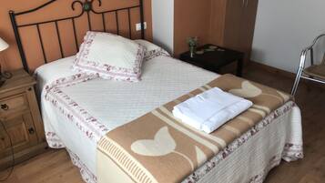 Una cama bien hecha con una colcha y almohadas de estampado floral, una manta marrón y una toalla blanca doblada sobre la cama.