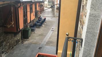 Una calle estrecha flanqueada por edificios, con mesas al aire libre y una planta en maceta.