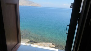 Vista a través de una puerta abierta hacia una zona costera con aguas cristalinas y montañas a lo lejos.