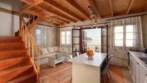 Un interior acogedor con una escalera de madera, un sofá, una mesa de centro de vidrio y una zona de cocina con vistas al mar.