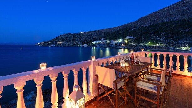 Una terraza con mesa y sillas que da a un mar tranquilo al atardecer.