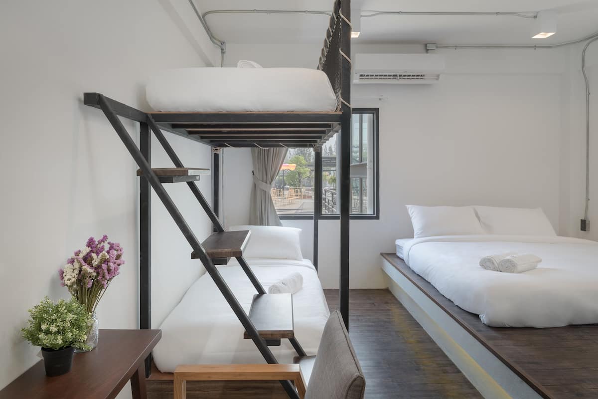 A bunk bed room with a window, a desk with a plant, and a bed with pillows.