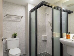 A modern bathroom with a glass-enclosed shower, a toilet, and a sink with toiletries. - Arch39 The Wall (Chiang Mai)