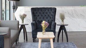 Una habitación moderna con un sillón tapizado oscuro, una mesita redonda con un jarrón de flores y una lámpara sobre una mesita auxiliar.