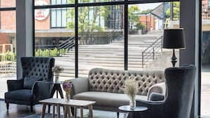 Un interior moderno con un sofá, sillones y una mesa de centro, ventanas amplias con vista a una escalera y un espacio exterior.
