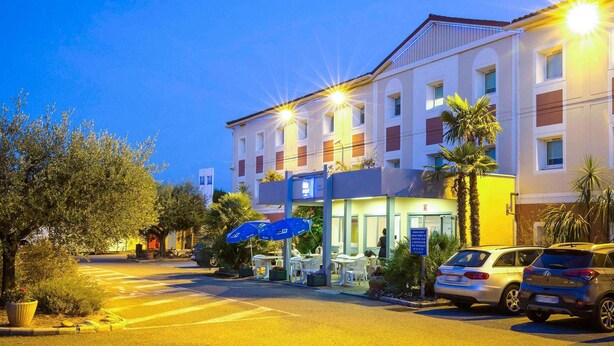 A hotel with a parking lot, outdoor seating, and a well-lit entrance.