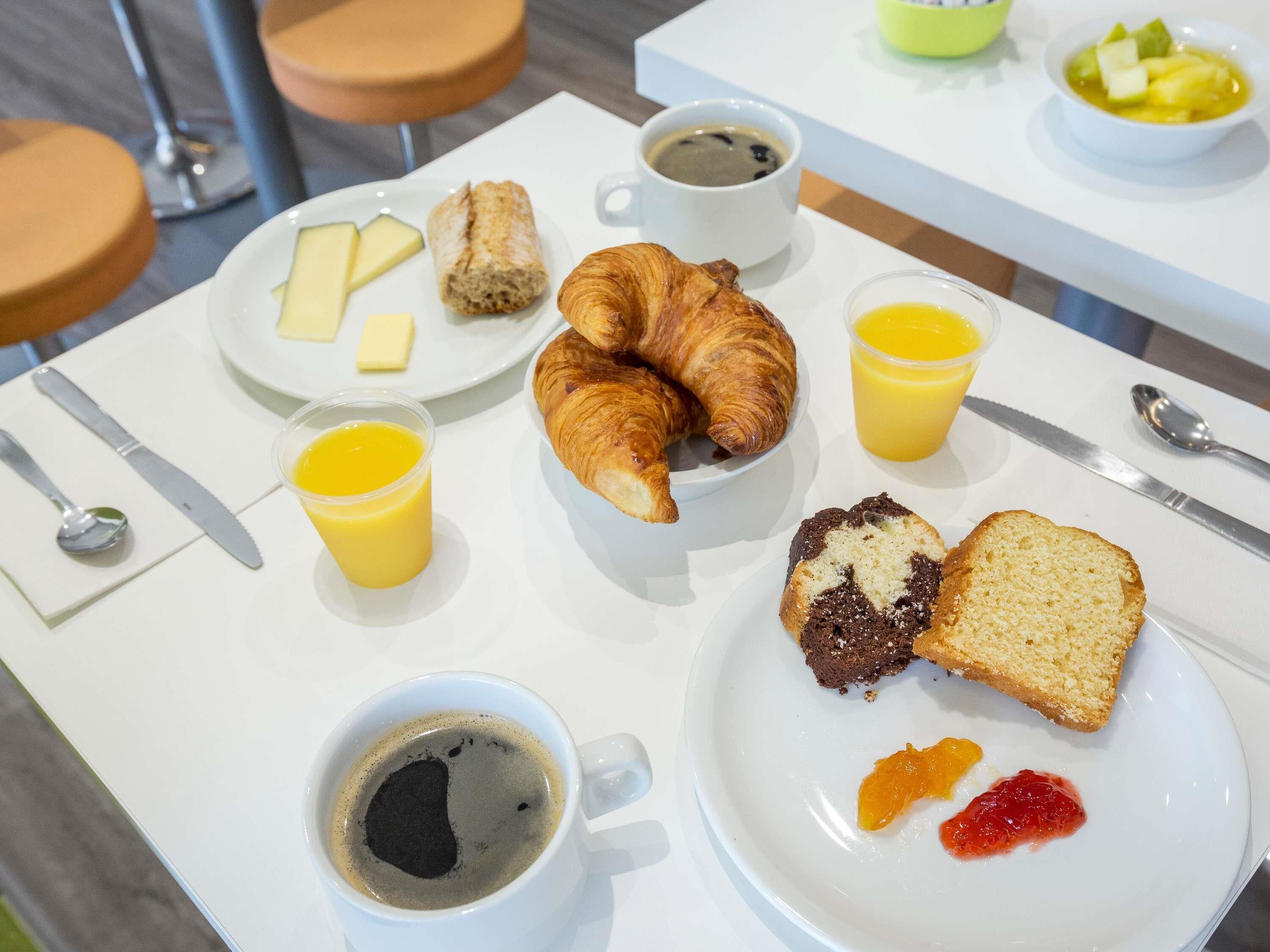 Une table dressée pour le petit-déjeuner, avec des croissants, des muffins, des toasts, des fruits, du café et du jus de fruits.
