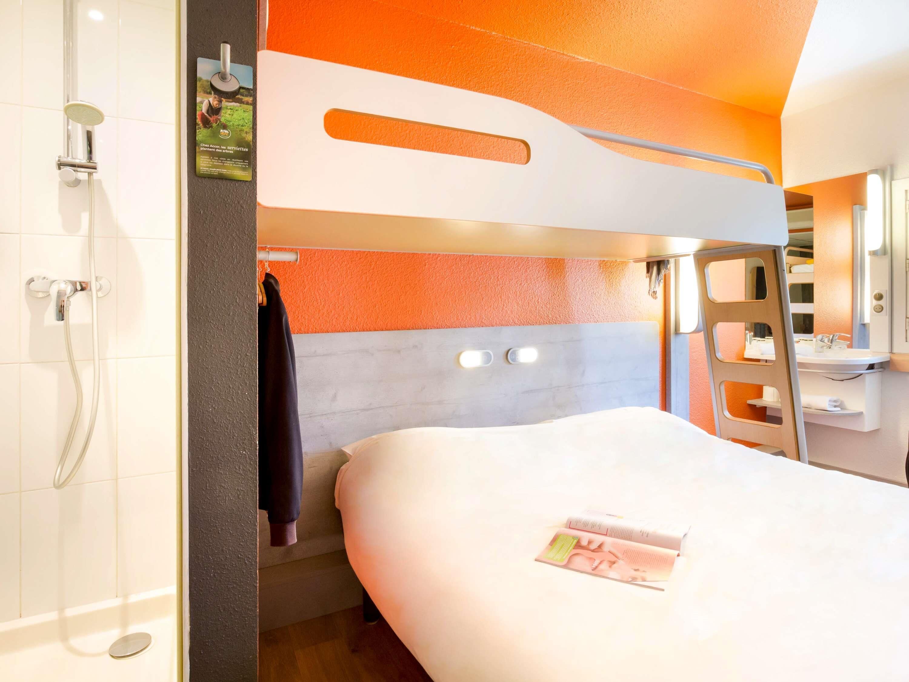 Ein modernes Hotelzimmer mit Stockbett, Dusche und einer kleinen Schreibtischzeile.