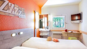 A hotel room with a bed, a bathroom with a sink and mirror, a TV mounted on the wall, and a window with a view of trees.