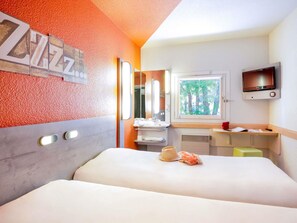 A hotel room with a bed, a bathroom with a sink and mirror, a TV mounted on the wall, and a window with a view of trees.