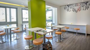 A modern cafe with high tables and orange stools, a green accent wall, and a decorative wall art piece.