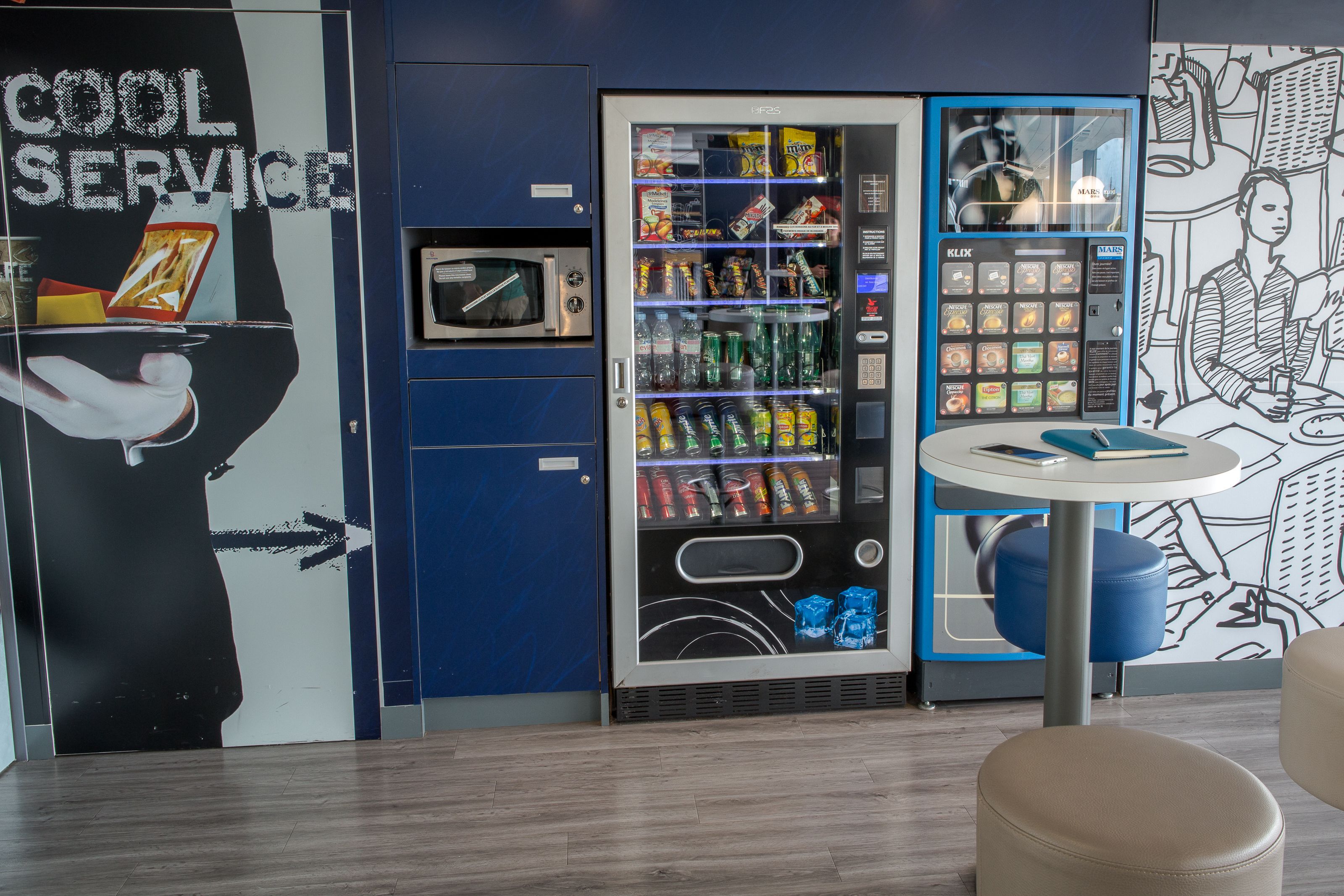 Een automaat met diverse snacks en dranken, een magnetron en een klein tafeltje met een stoel.