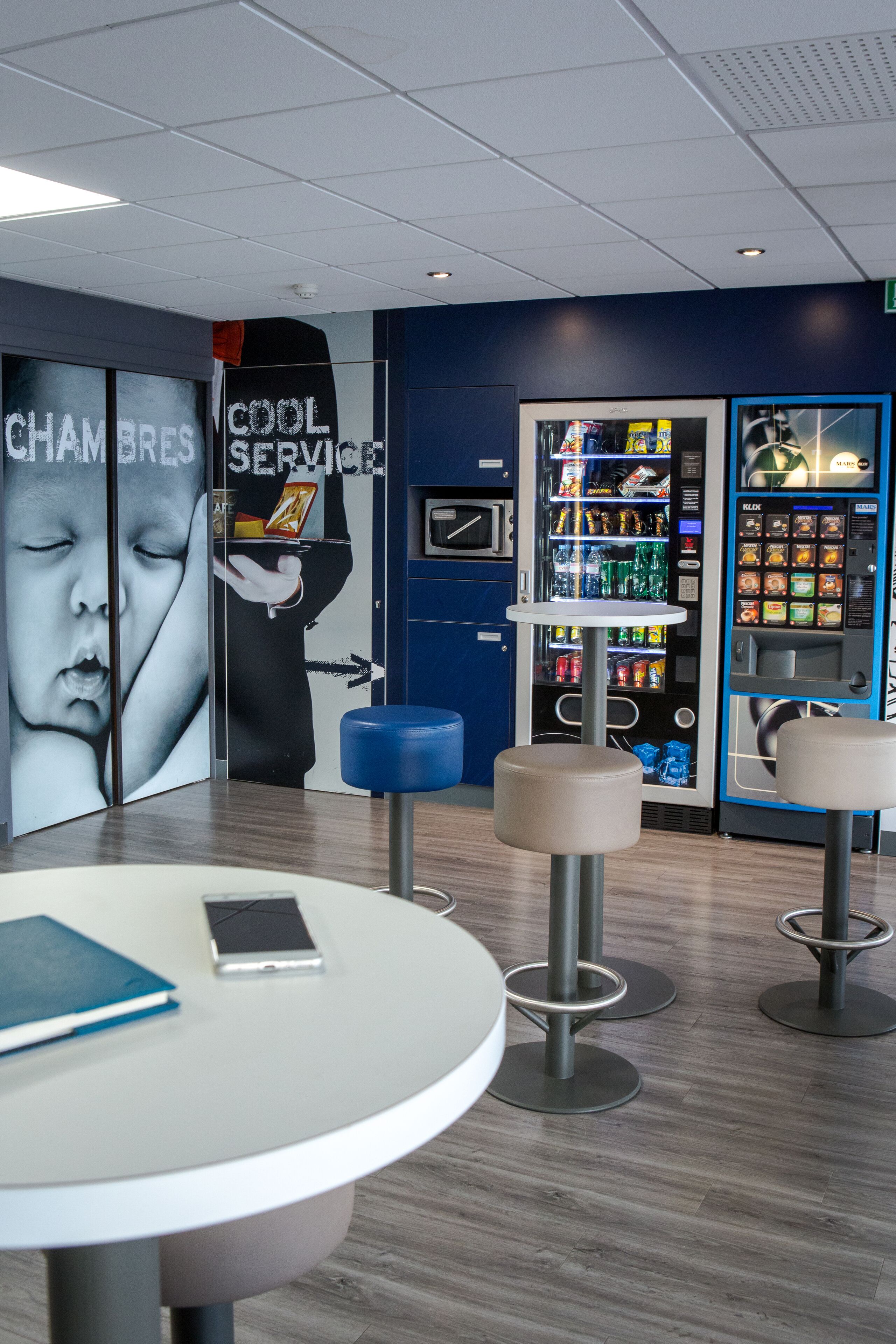 A modern interior with a vending machine, a table with a smartphone, and bar stools.