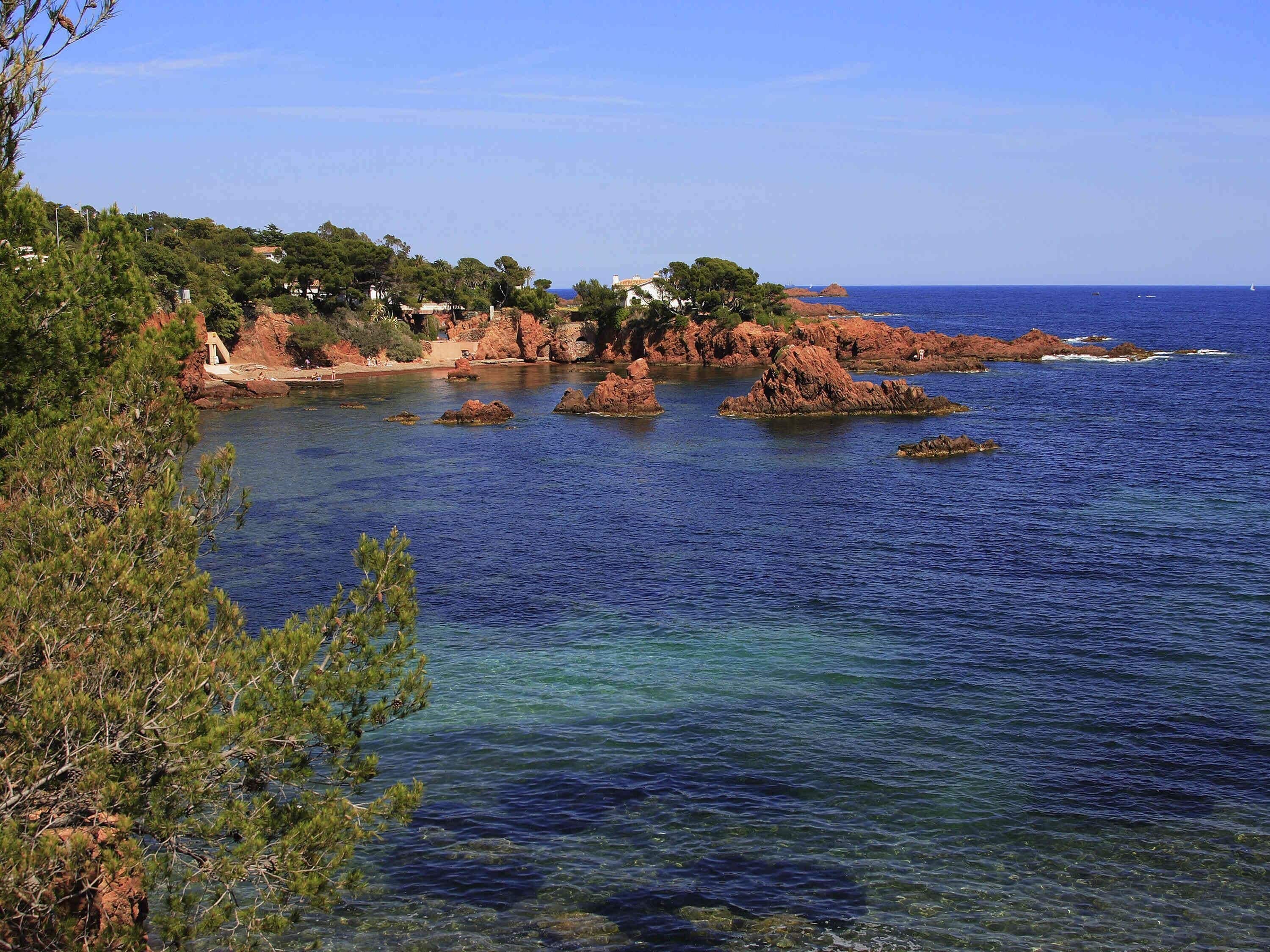 A coastal landscape with clear blue waters, rocky outcrops, and dense greenery.