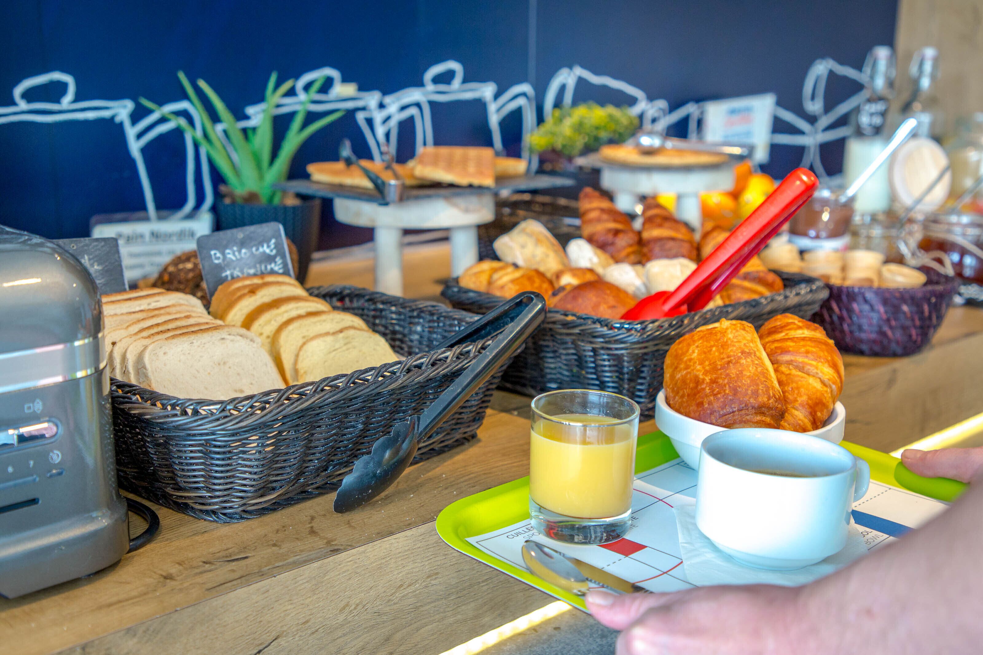 Un buffet de petit-déjeuner proposant différentes sortes de pains, des croissants et un verre de jus d’orange.