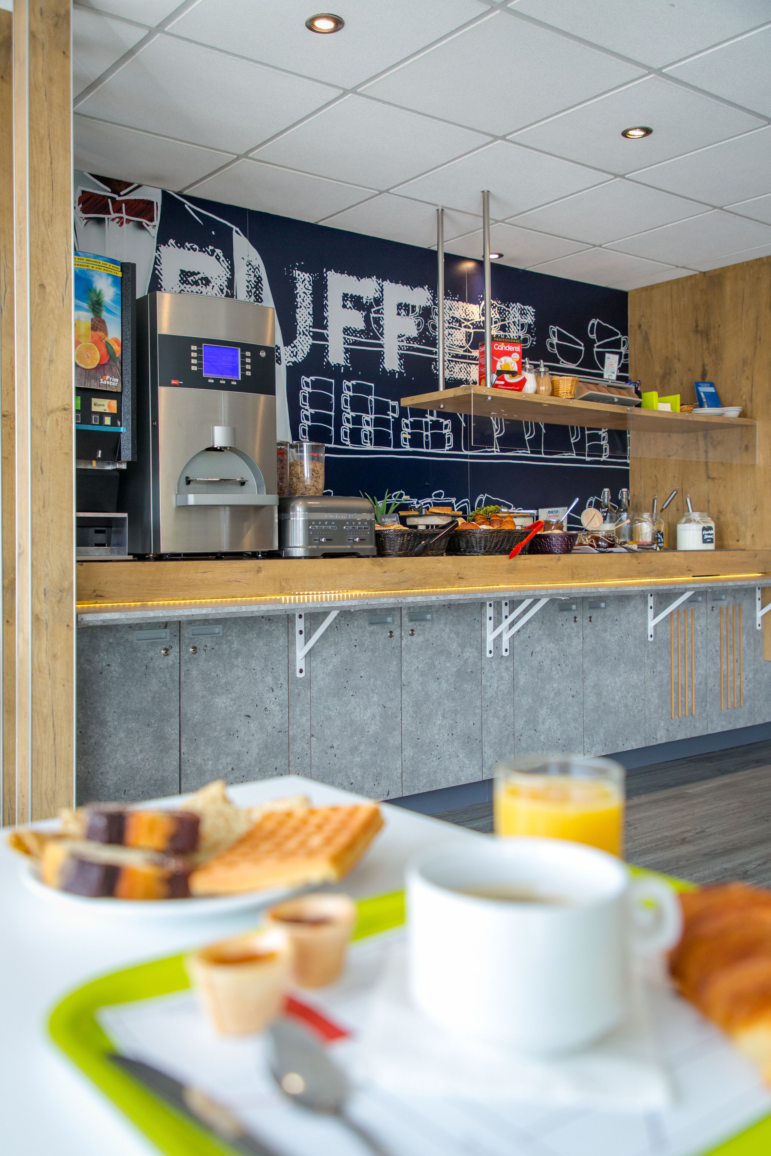 Frühstückstisch mit Waffeln, Kaffee und Saft in einer modernen Küchenzeile, inklusive Kaffeemaschine und einer Tafel.