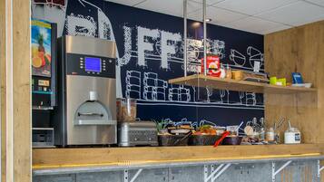Frühstückstisch mit Waffeln, Kaffee und Saft in einer modernen Küchenzeile, inklusive Kaffeemaschine und einer Tafel.